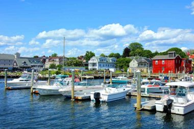 Boats in the harbor with quant coastal building painted white, red, and blue behind them in the beach town of Bristol.
