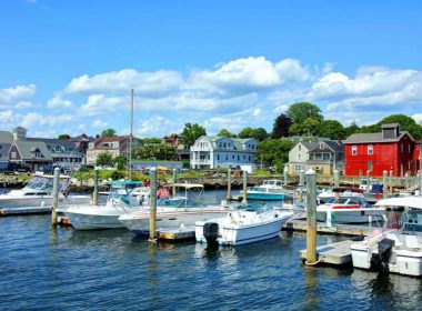 Boats in the harbor with quant coastal building painted white, red, and blue behind them in the beach town of Bristol.