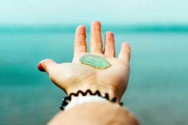 Holding up a piece of smooth aqua sea glass matching the color of the ocean water in the distance.