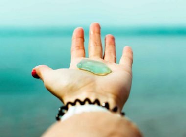 Holding up a piece of smooth aqua sea glass matching the color of the ocean water in the distance.