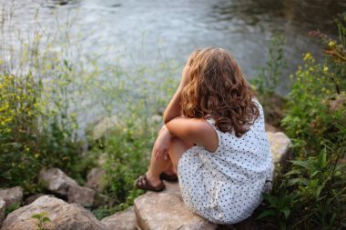 A woman sits on rocks near the edge of a lake, looking at the water.