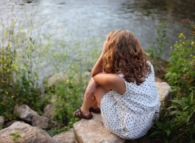 A woman sits on rocks near the edge of a lake, looking at the water.