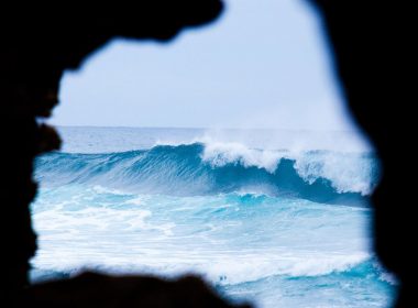 View from a dark chasm carved by the ocean, beautiful blue waves thunder toward the shoreline.