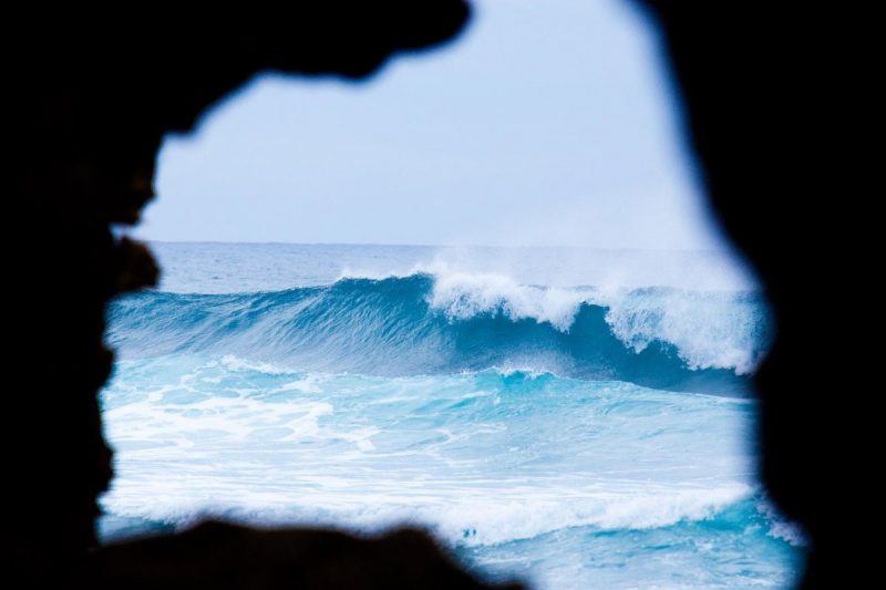 View from a dark chasm carved by the ocean, beautiful blue waves thunder toward the shoreline.